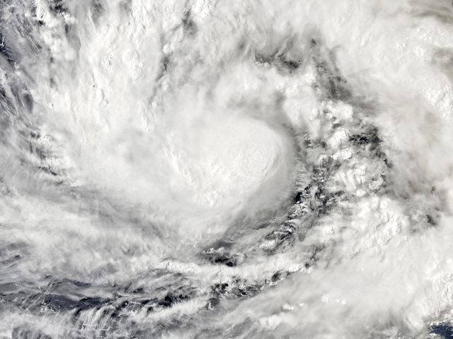 True-colour satellite image of a large spiral of white cloud over dark blue ocean, with a dense, tightly wound centre and long curved cloud bands; no land is clearly visible.